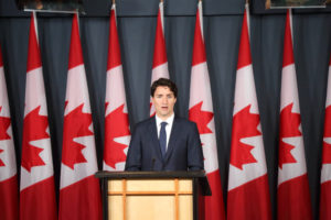 Il primo ministro canadese Justin Trudeau dietro a un podio davanti a nove bandiere canadesi. Si va verso il divieto di detenzione di armi d'assalto e di pistole.
