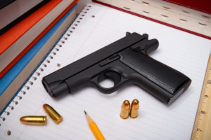 pistola con munizioni su blocco per appunti accanto a lapis: fondi federali per armare gli insegnanti