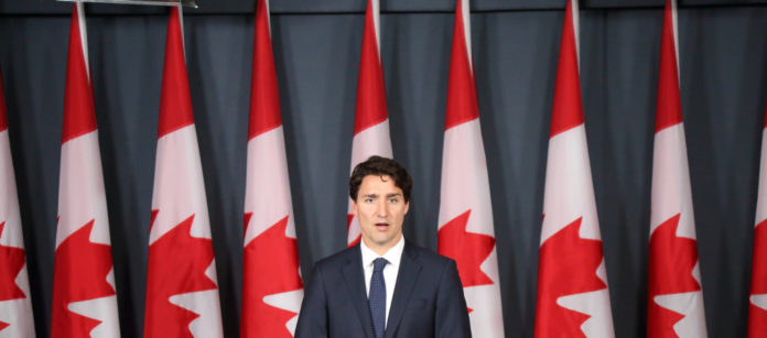 Il primo ministro canadese Justin Trudeau dietro a un podio davanti a nove bandiere canadesi. Si va verso il divieto di detenzione di armi d'assalto e di pistole.