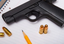 Il governo statunitense valuta l’utilizzo di fondi federali per armare gli insegnanti pistola con munizioni su blocco per appunti accanto a lapis: fondi federali per armare gli insegnanti