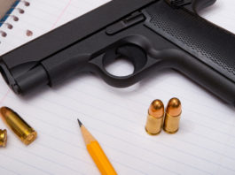 Il governo statunitense valuta l’utilizzo di fondi federali per armare gli insegnanti pistola con munizioni su blocco per appunti accanto a lapis: fondi federali per armare gli insegnanti