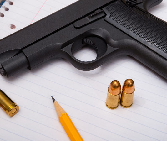 Il governo statunitense valuta l’utilizzo di fondi federali per armare gli insegnanti pistola con munizioni su blocco per appunti accanto a lapis: fondi federali per armare gli insegnanti