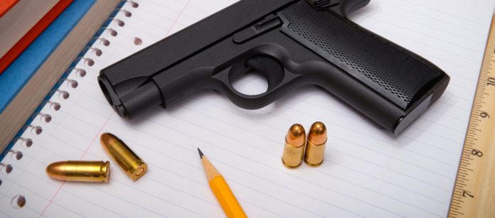 pistola con munizioni su blocco per appunti accanto a lapis: fondi federali per armare gli insegnanti