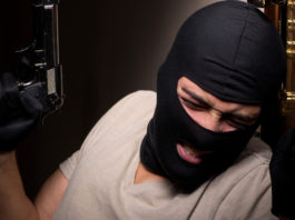 Riforma della legittima difesa: ecco gli emendamenti al testo base rapinatore appoggiato a una porta con pistola e passamontagna