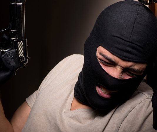 Riforma della legittima difesa: ecco gli emendamenti al testo base rapinatore appoggiato a una porta con pistola e passamontagna