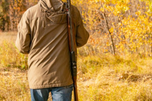 Specie cacciabili: cacciatore nel bosco, di spalle, con fucile a tracolla
