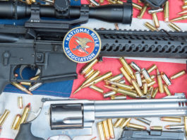 Slitta ancora la data della convention Nra data della convention Nra: armi e proiettili su bandiera americana con sticker Nra