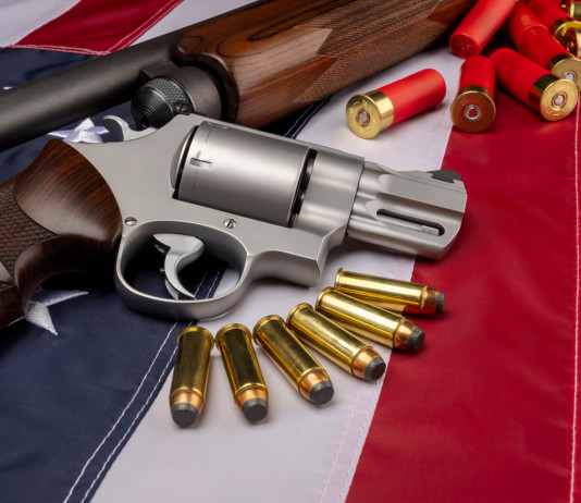 Background check richiesti in America, il dato finale del 2021 Background check richiesti in America: revolver e fucile con munizioni su bandiera americana