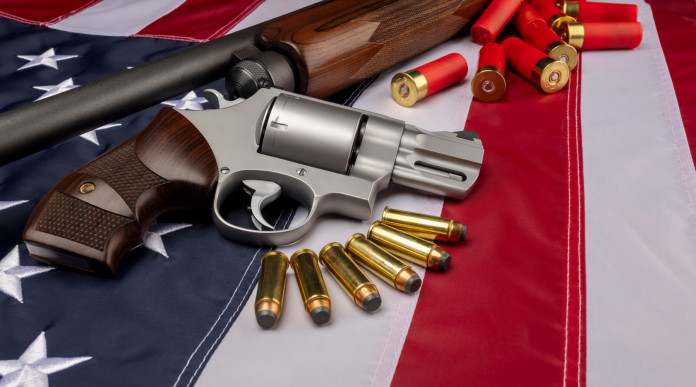 Background check richiesti in America: revolver e fucile con munizioni su bandiera americana