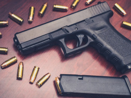 Scadenza del porto d’armi e stato d’emergenza: che succede? Scadenza del porto d’armi e stato d'emergenza: pistola Glock su tavolo di legno con munizioni