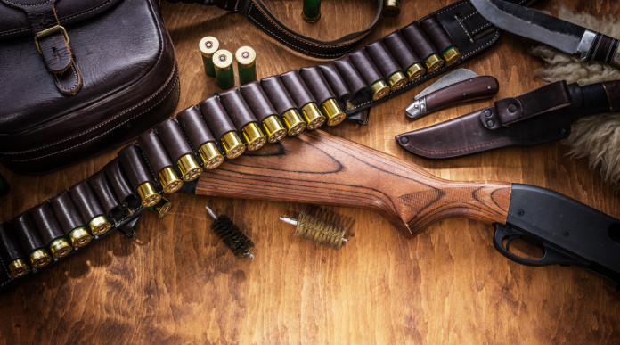 Reati e preclusione automatica del porto d’armi: fucile a pompa e cartucce su tavolo di legno