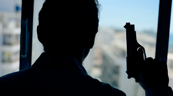 Licenza per uso sportivo e difesa personale: uomo davanti alla finestra, di spalle, con pistola in mano