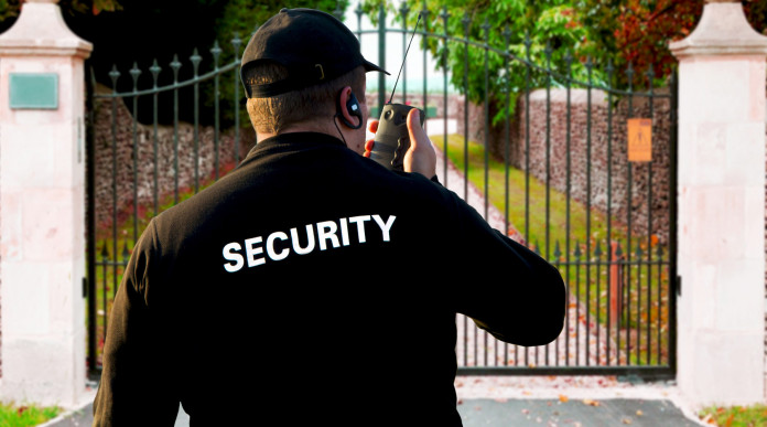 Revoca del porto d’armi a guardia giurata: security guard di spalle davanti al cancello di una villa