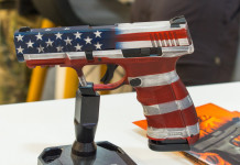 Mercato delle armi in America: i dati finali del 2023 Mercato delle armi in America, i dati finali del 2023: pistola con bandiera americana esposta a fiera delle armi