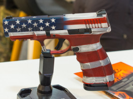 Mercato delle armi in America: i dati finali del 2023 Mercato delle armi in America, i dati finali del 2023: pistola con bandiera americana esposta a fiera delle armi